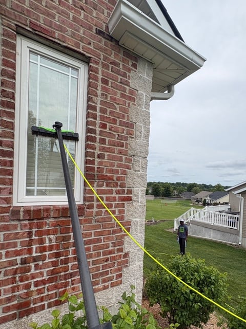 Bright yellow extension cord strung from a brick house corner to a person standing in a grassy yard with trees and other houses visible in the background.