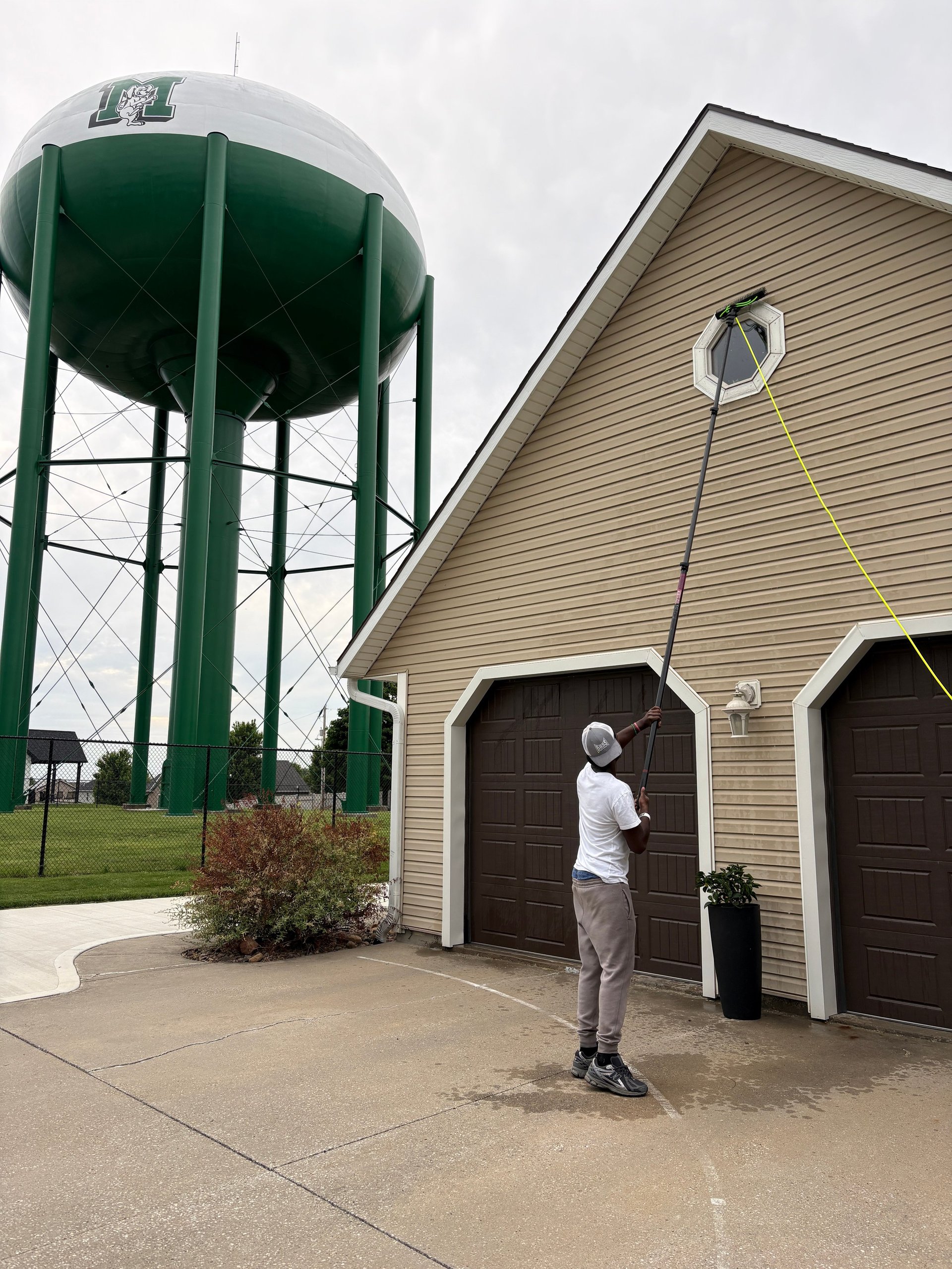 Person standing near a tan building with dark garage doors next to a tall green water tower on concrete pavement
